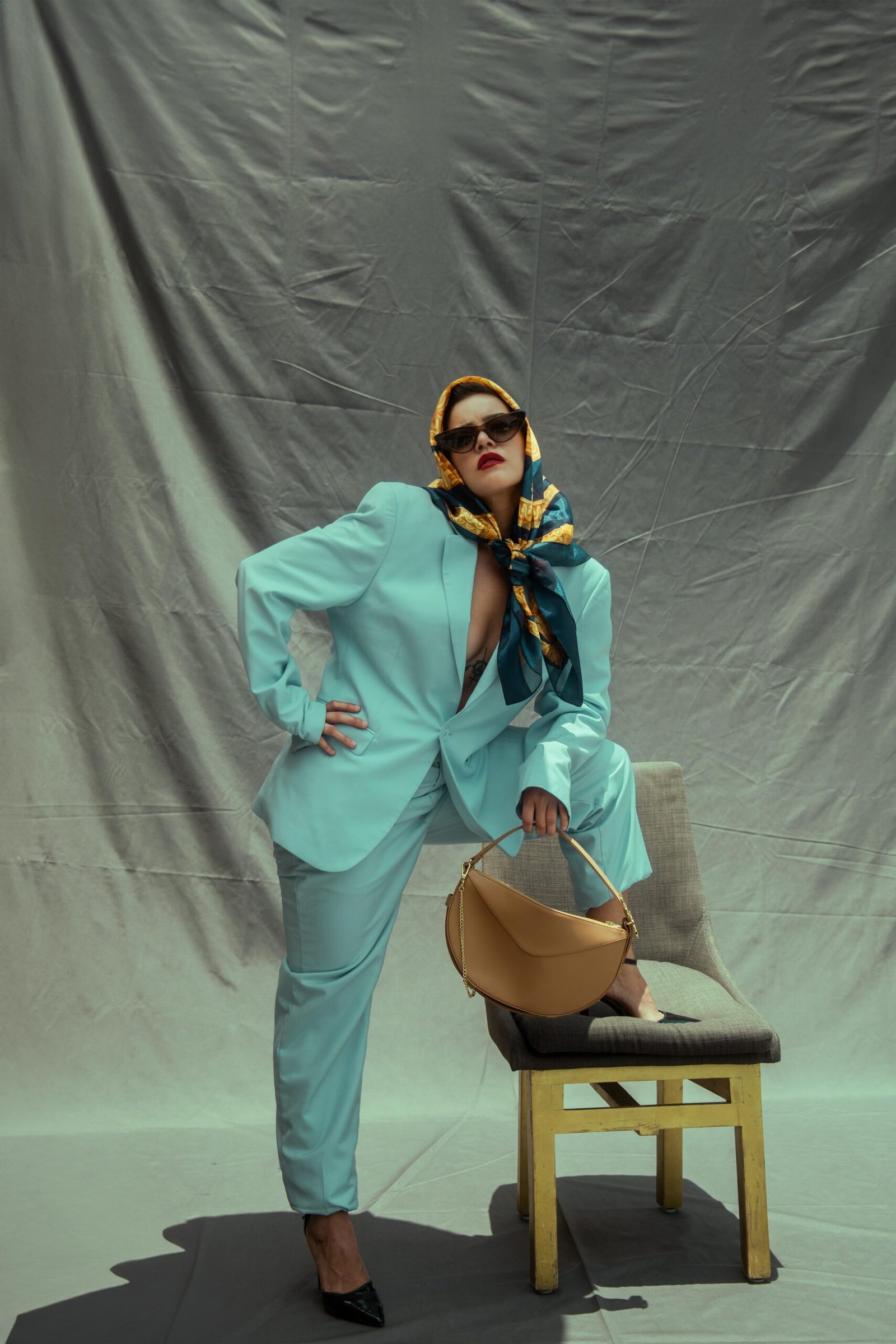 Stylish woman in a pastel suit posing with a chair and handbag indoors.