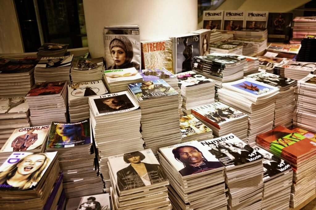 pexels-photo-264600-264600 Huge stacks of diverse fashion and lifestyle magazines piled high in an indoor store setting.